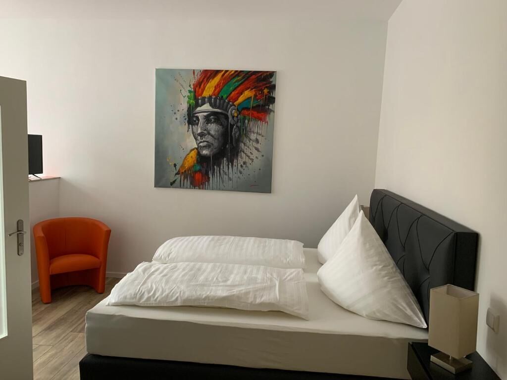 Ein Schlafzimmer mit Bett, Sessel, Nachttisch und einem Wandbild.