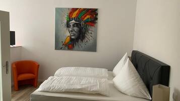 Ein Schlafzimmer mit Bett, Sessel, Nachttisch und einem Wandbild.