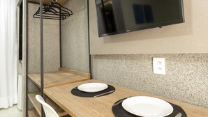 A modern room with a bunk bed, a flat-screen TV mounted on the wall, a wooden dining table with two white plates and a black placemat, and a white chair with yellow legs. - Liiv Cobogó - Natal Ponta Negra (Natal)