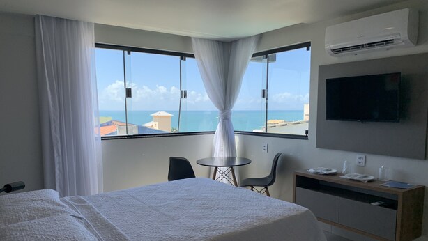 A hotel room with a bed, a desk, a chair, a TV, and a view of the sea. - Liiv Cobogó - Natal Ponta Negra (Natal)