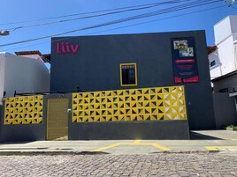 Um edifício com um letreiro 'Liiv' em destaque, uma cerca amarela com padrão geométrico e uma pequena janela.