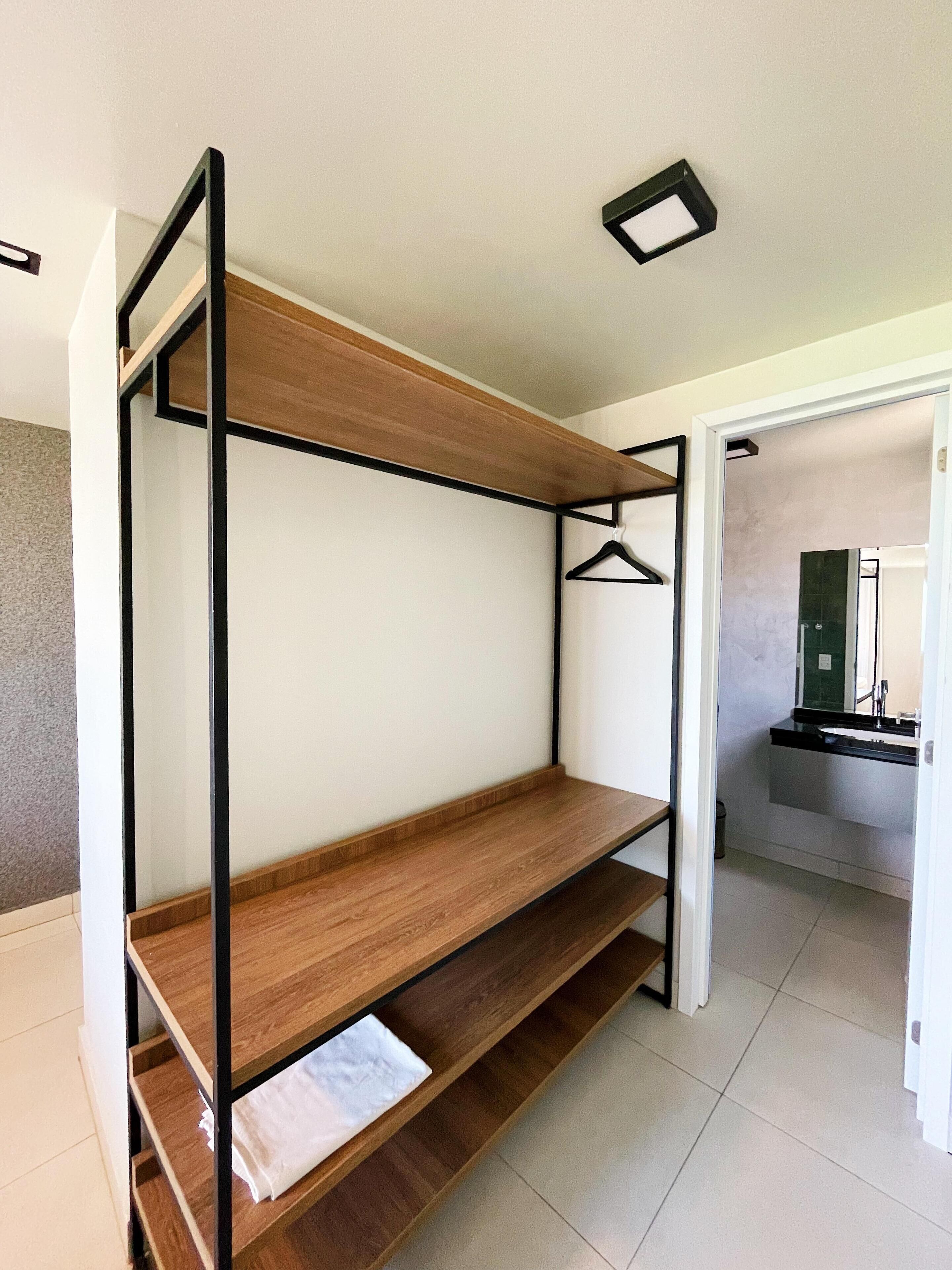 A bunk bed with wooden slats and black metal frames in a room with a tiled floor and a bathroom visible in the background.