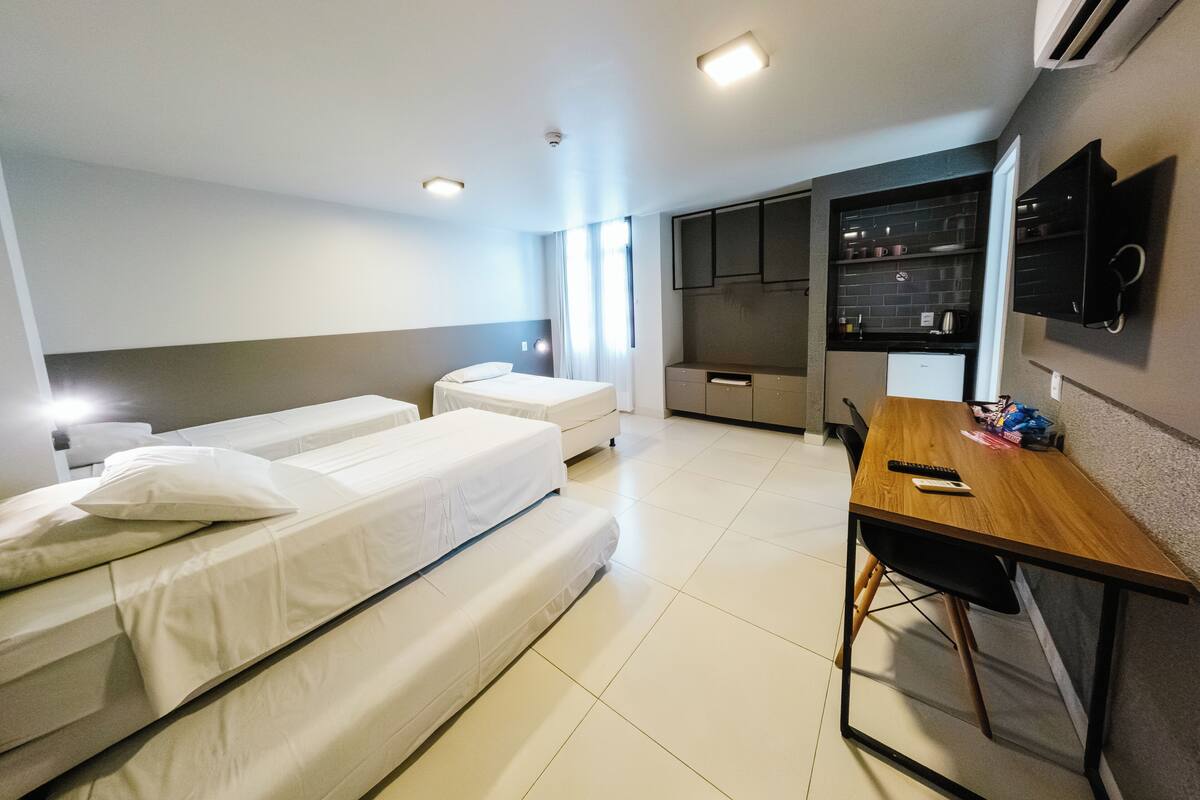 Una habitación de hotel con dos camas, un escritorio, kitchenette y un televisor montado en la pared.