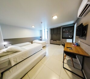 Quarto de hotel com duas camas, uma mesa de escritório, uma cozinha compacta e uma televisão presa à parede.