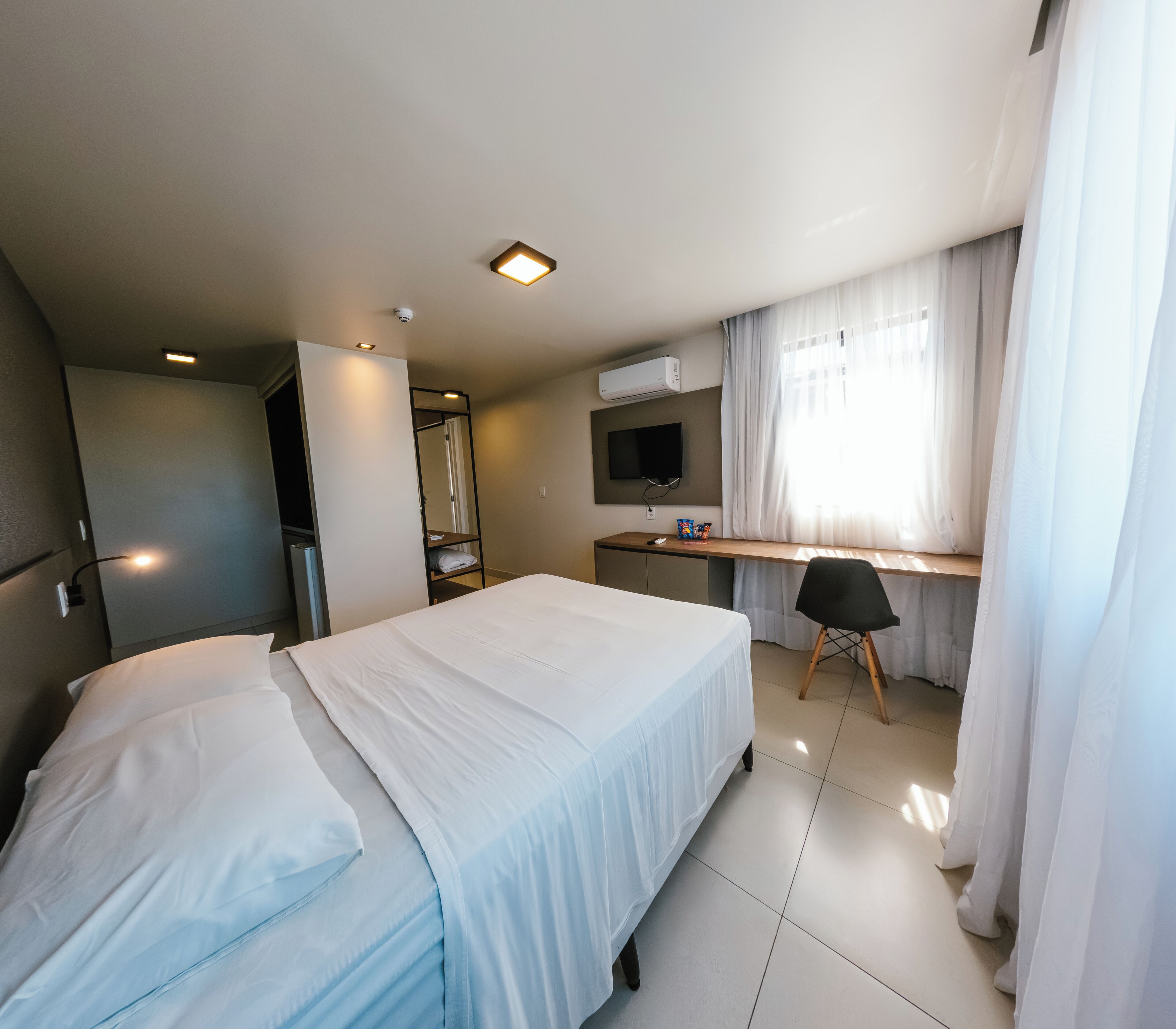 Una habitación de hotel con cama, escritorio, silla, televisor y aire acondicionado.