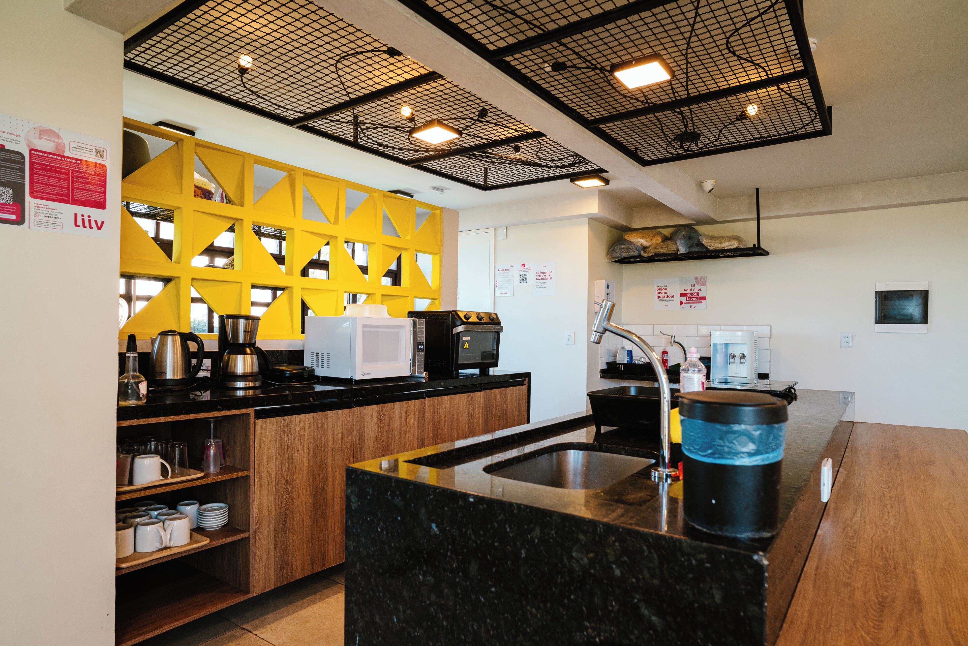 A modern kitchen with a black granite countertop, a yellow geometric wall, and a black ceiling grid.