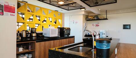 A modern kitchen with a black granite countertop, a yellow geometric wall, and a black ceiling grid.
