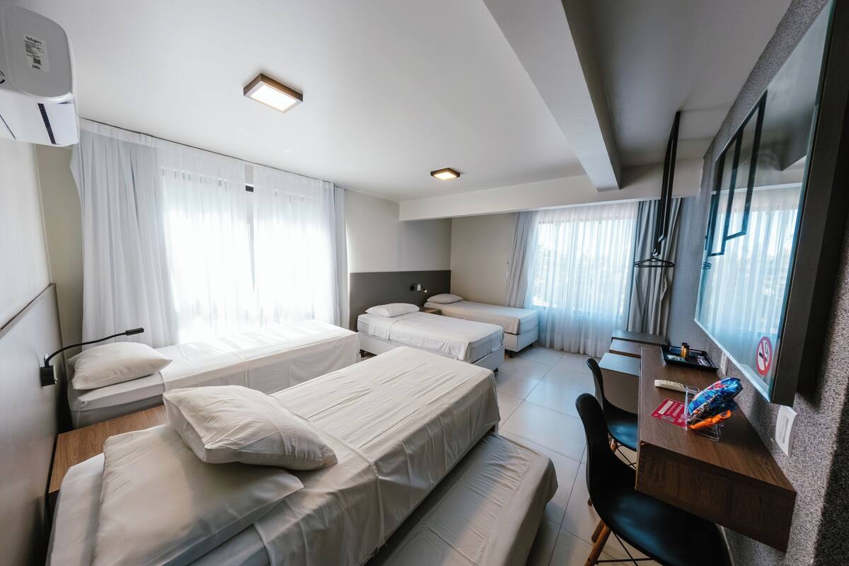 Habitación de hotel con dos camas, un escritorio, una silla, un televisor y una ventana con cortinas.