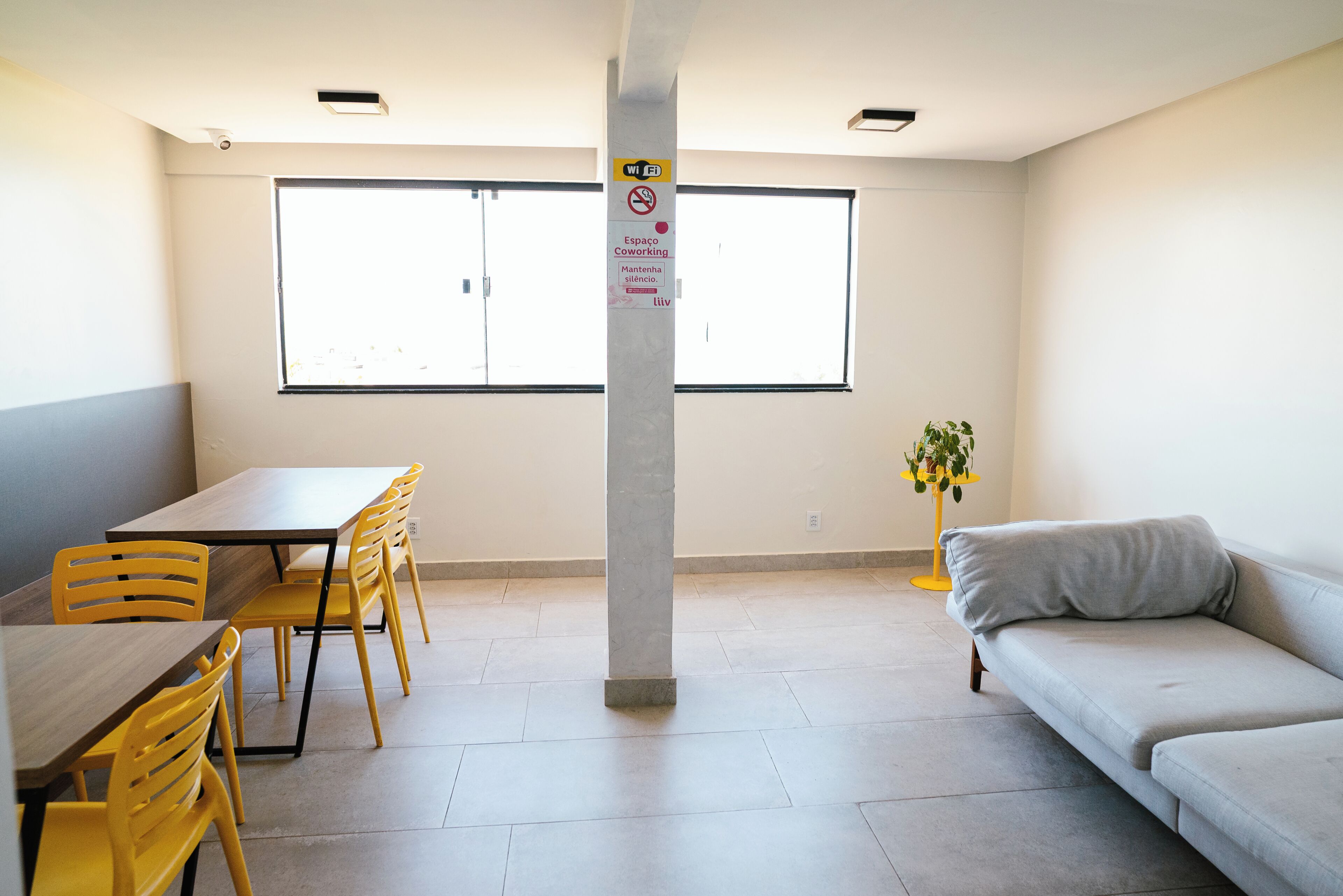 Ein Zimmer mit Esstisch, Stühlen, einer Couch, einer Säule mit Schildern und einem Fenster.