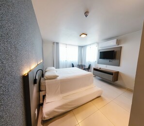 Quarto de hotel moderno com cama, televisão, escrivaninha e cadeira.