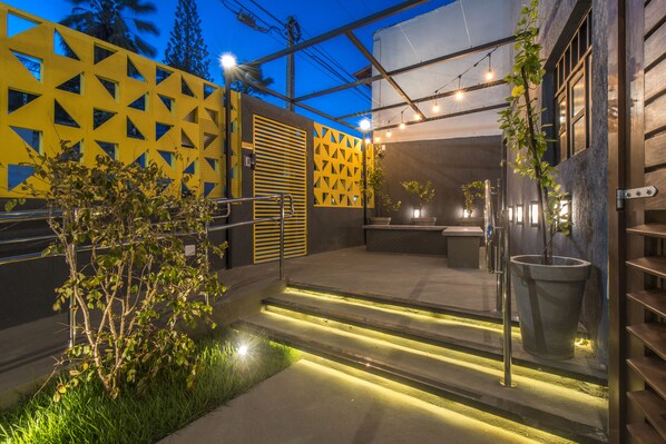 Uma área externa moderna com padrões geométricos na parede, um pequeno espelho d'água e iluminação ambiente.