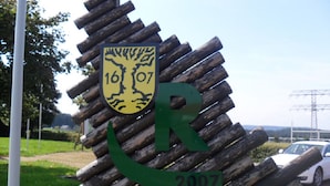 Uma estrutura de madeira com um brasão e a letra 'R'.