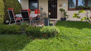 Uma casa com um alpendre, um guarda-sol vermelho, uma mesa com cadeiras e um vaso de planta.