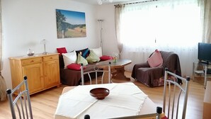 Uma sala de estar com uma mesa de jantar de madeira, um sofá, uma televisão e um quadro na parede.
