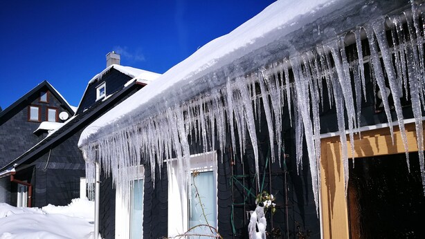 Uma casa com icicles pendurados no telhado, rodeada por neve.