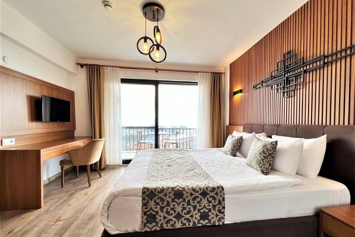 Ein Hotelzimmer mit einem großen Bett, einem Schreibtisch, einem Fernseher und einem Balkon mit Blick.