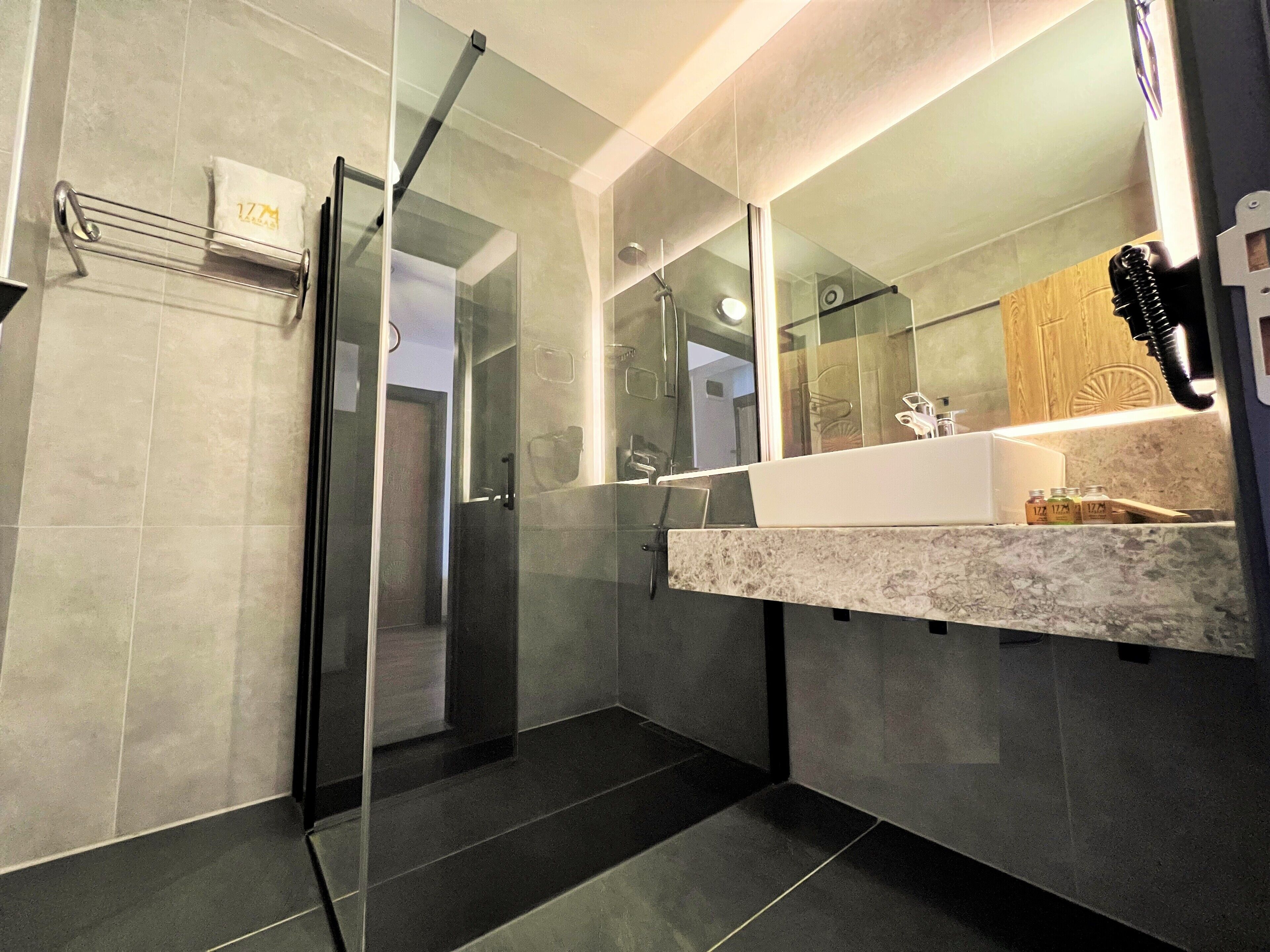 Un baño moderno con cabina de ducha de vidrio, encimera de mármol y un espejo grande.