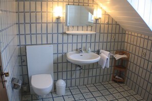 A small, tiled bathroom with a toilet, sink, and mirror. - Haus Wegener (Bad Sassendorf)