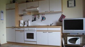 Uma cozinha compacta com armários brancos, fogão, micro-ondas e televisão.