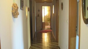 Um corredor com piso estampado, teto de madeira e porta para um banheiro.