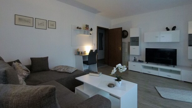A modern living room with a sectional sofa, a coffee table, a TV, and a bookshelf. - Ferienwohnung Auszeit (Hofheim in Unterfranken)