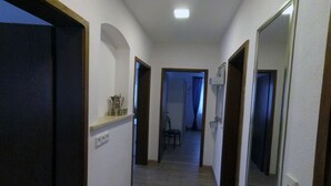 A hallway with a wooden floor, white walls, and a ceiling light. There are doors on both sides, and a chair is visible in the distance. - Ferienwohnung Auszeit (Hofheim in Unterfranken)