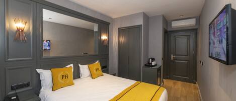 A hotel room with a large bed, a bedside table with a phone, a mirror, a television, and a door leading to another room.