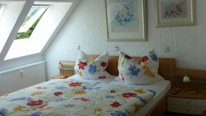 A bedroom with a sloped ceiling, skylights, a bed with floral bedding, two framed pictures, and a bedside table with a lamp. - Fewo im Josefinum (Bad Sassendorf)