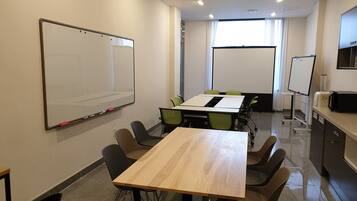 Un salón de conferencias con una gran mesa, sillas, una pizarra y una pantalla para proyector.