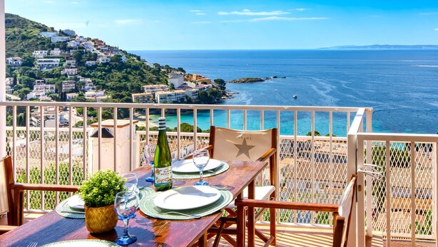 A terrace with a table set for two, overlooking a coastal town and the sea. - MALLORCA 8 Canyelles Roses (Rosas / Roses)