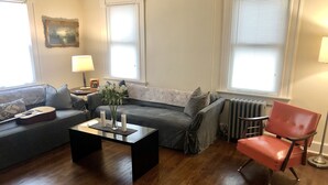 Een woonkamer met een grijze bank, een zwarte salontafel, een rode stoel en een gitaar.