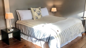 Een slaapkamer met een bed, twee nachtkastjes, een lamp op elk nachtkastje en een houten vloer.