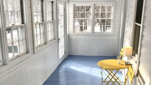 Een kamer met witte wanden, een blauwe vloer en een gele tafel met stoelen. Er zijn ramen met witte kozijnen en een radiator aan de muur.