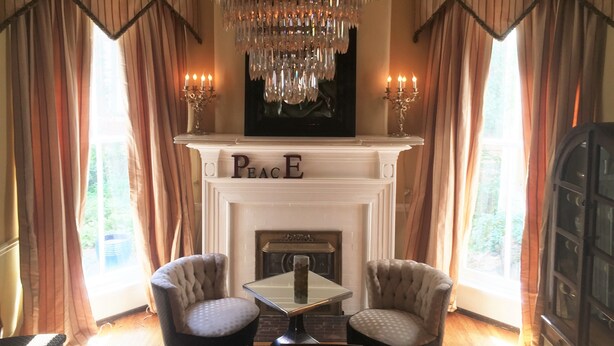 A room with a fireplace, two armchairs, a table, and a chandelier. - Historic Mansion-Modern Amenities, Sauna, Fire Pit, Hot Tub, Deck, Walk to Dine (Louisville)