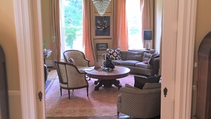 A spacious living room with a chandelier, a sofa, a coffee table, and a dining area with a patterned table runner. - Historic Mansion-Modern Amenities, Sauna, Fire Pit, Hot Tub, Deck, Walk to Dine (Louisville)