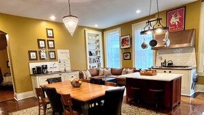A kitchen with a dining area, featuring a chandelier, a coffee maker, and a refrigerator. - Historic Mansion-Modern Amenities, Sauna, Fire Pit, Hot Tub, Deck, Walk to Dine (Louisville)