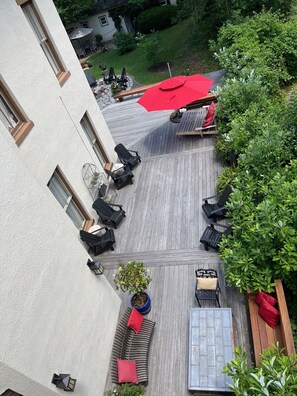 Une terrasse sur le toit avec des sièges en plein air, un parasol rouge et des plantes en pot.