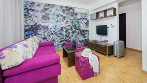 A modern living room with a vibrant purple sofa, a wooden coffee table, and a decorative wall with floral wallpaper. - One Bedroom Apartment with Sea View (Pržno)