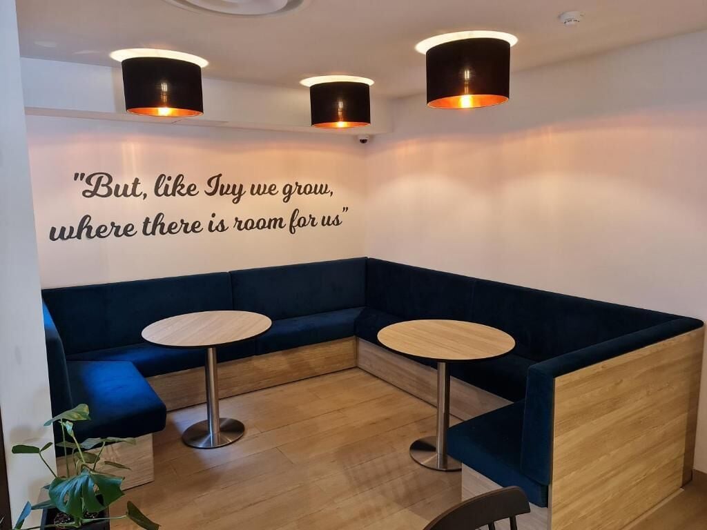 Ein moderner Lounge-Bereich mit einem gewölbten blauen Sofa, zwei runden Holztischen und einer Wandspruch.
