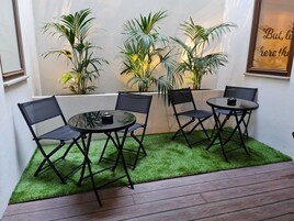 Un patio con una mesa redonda y cuatro sillas, rodeado de césped artificial y plantas en macetas.