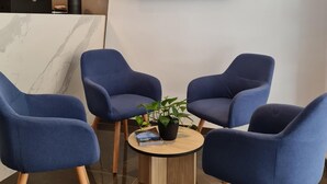 A reception area with a modern design, featuring a marble reception desk, a large screen displaying the hotel name, and a seating area with blue chairs and a small round table with a plant. - Ivy Hotel - Adults Only (St. Julian's)