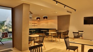 A modern hotel dining area with wooden tables and chairs, a large TV on the wall, and a sign with a quote. - Ivy Hotel - Adults Only (St. Julian's)