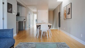 A modern living room with a dining table and chairs, a sofa, and a kitchen in the background.