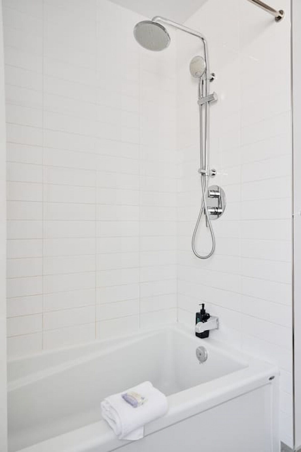 A modern bathroom with a white tiled wall, a freestanding bathtub, and a shower with a handheld showerhead and a wall-mounted faucet.