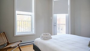 A bedroom with a bed, a chair, and two windows.