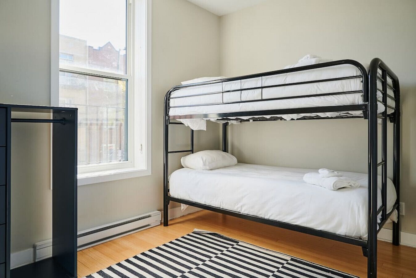 A bunk bed in a room with a window, a radiator, and a striped rug.