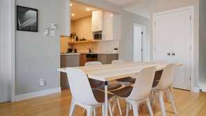 A modern kitchen with white cabinets, a wooden countertop, and a dining area with a wooden table and white chairs.