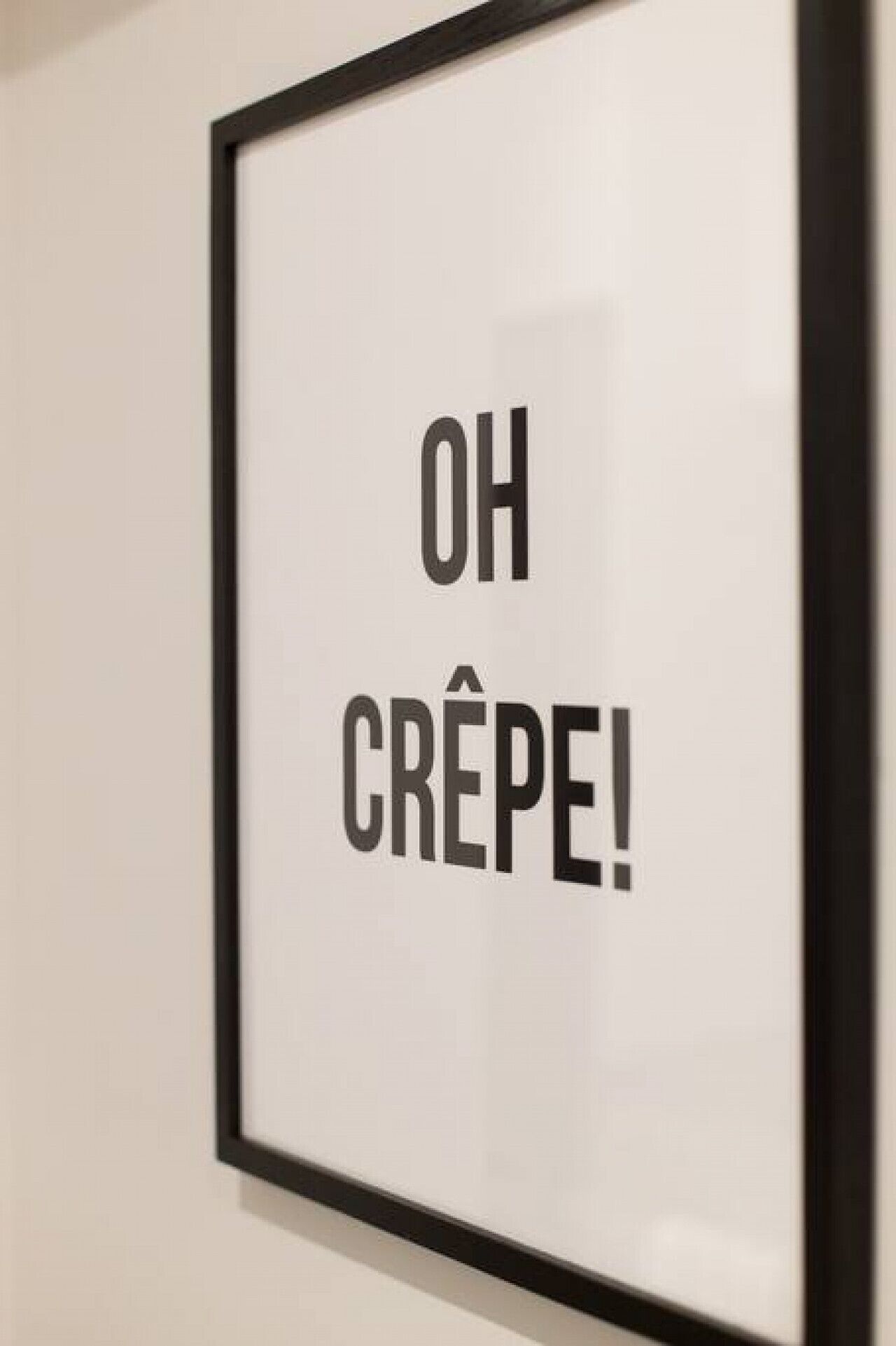 Une affiche encadrée avec l’inscription « OH CRÊPE ! » sur un mur uni.