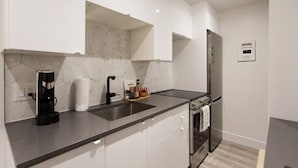 A modern kitchen with white cabinets, a black countertop, a stainless steel refrigerator, and a built-in oven.
