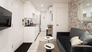 A compact living space with a kitchenette, a sofa, a coffee table, and a TV mounted on the wall.